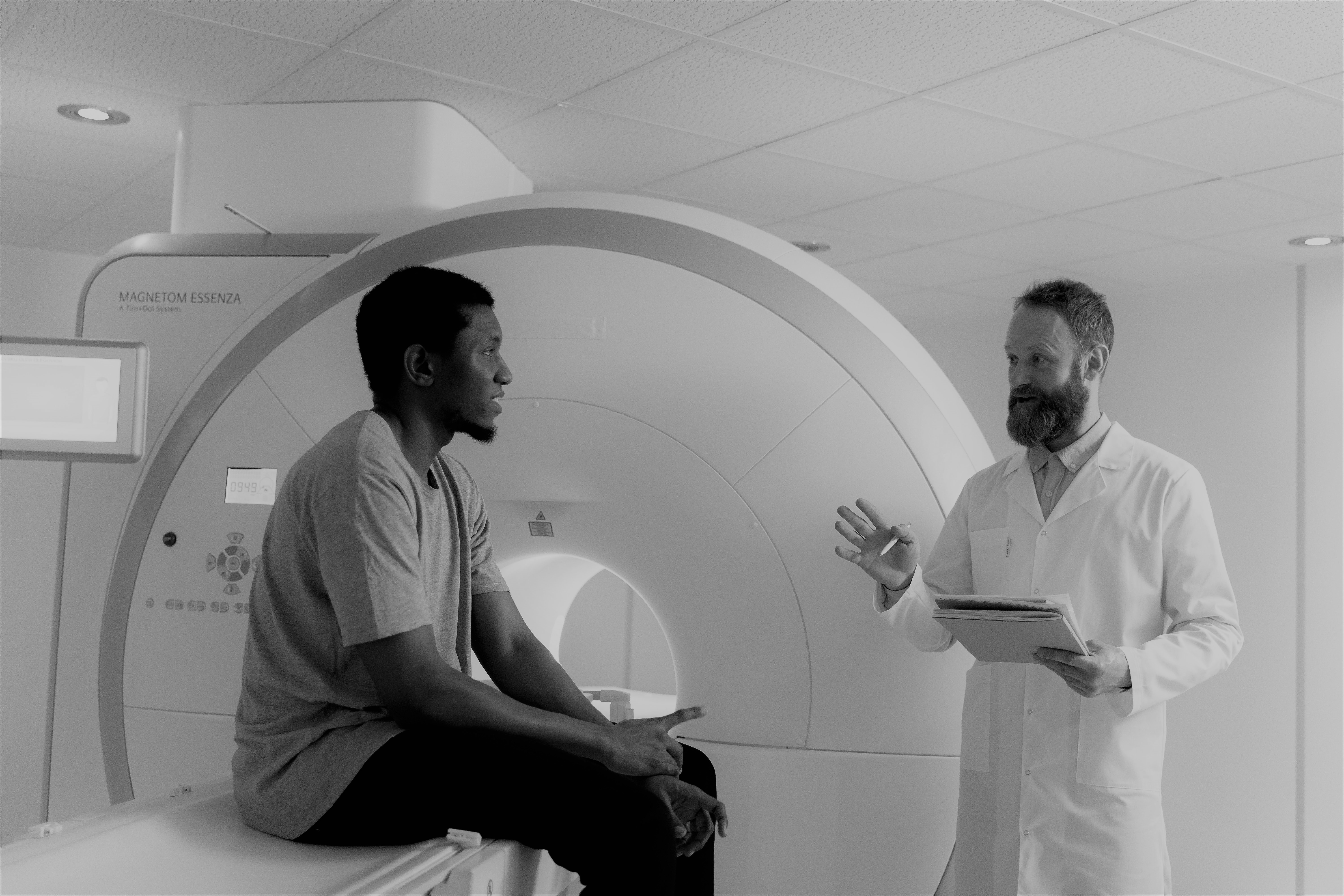 Person sitting on a CT scan machine is talking to a person in a white coat with a clipboard