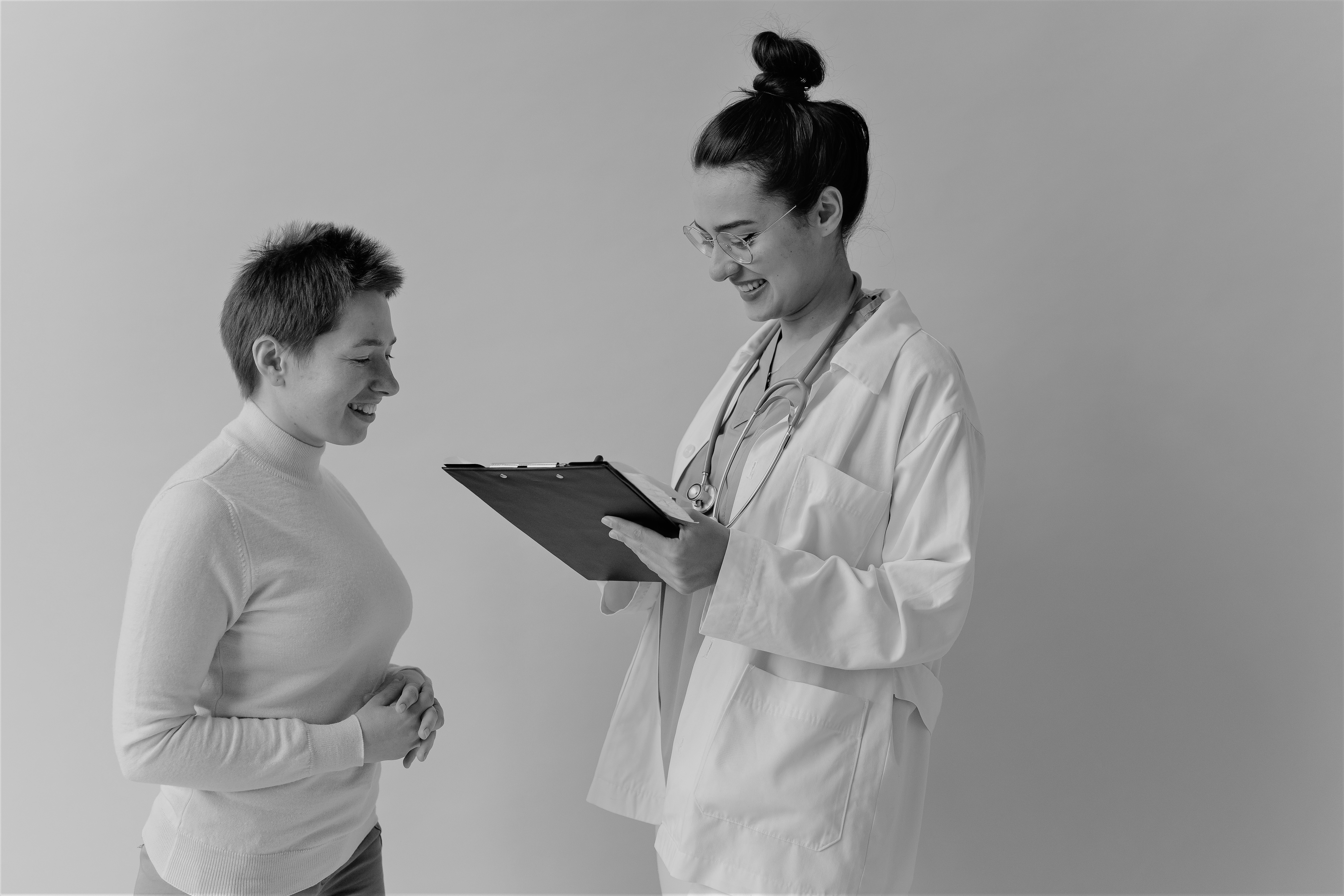 Doctor with hair up and a clipboard is smiling at a person standing in front of them
