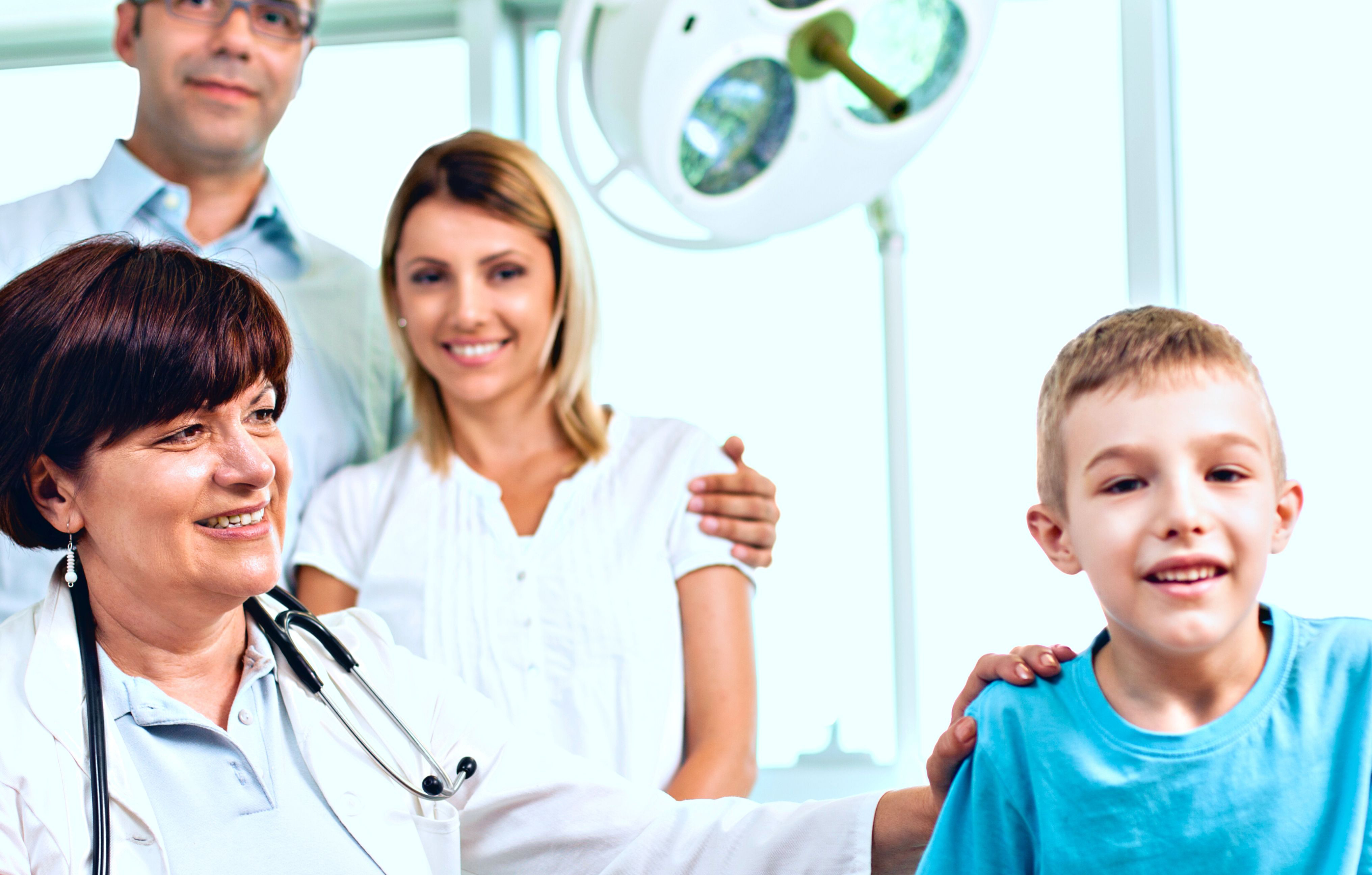 Parents standing behind a doctor who is seated next to a young child who is smiling