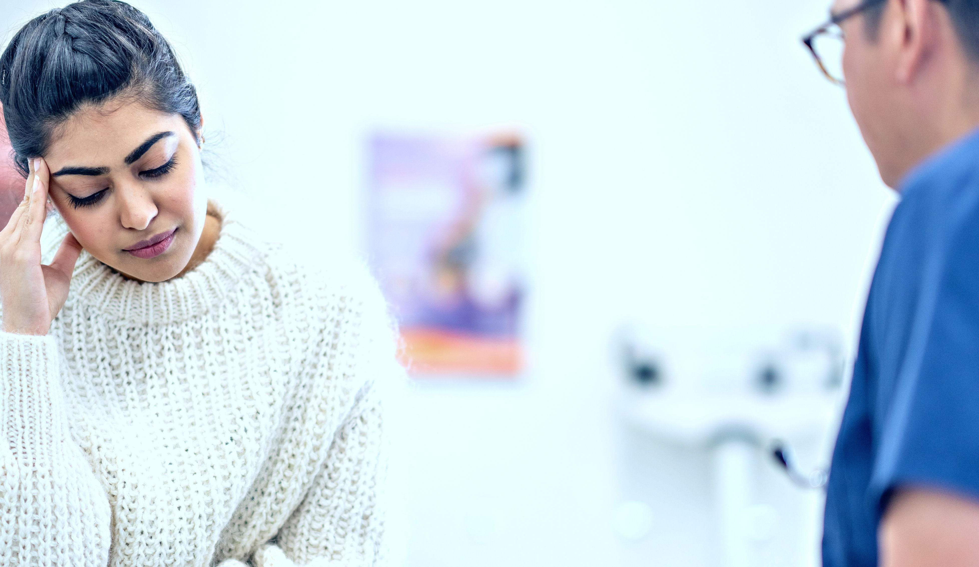 young person with head leaning on hand in white sweater sitting across from doctor